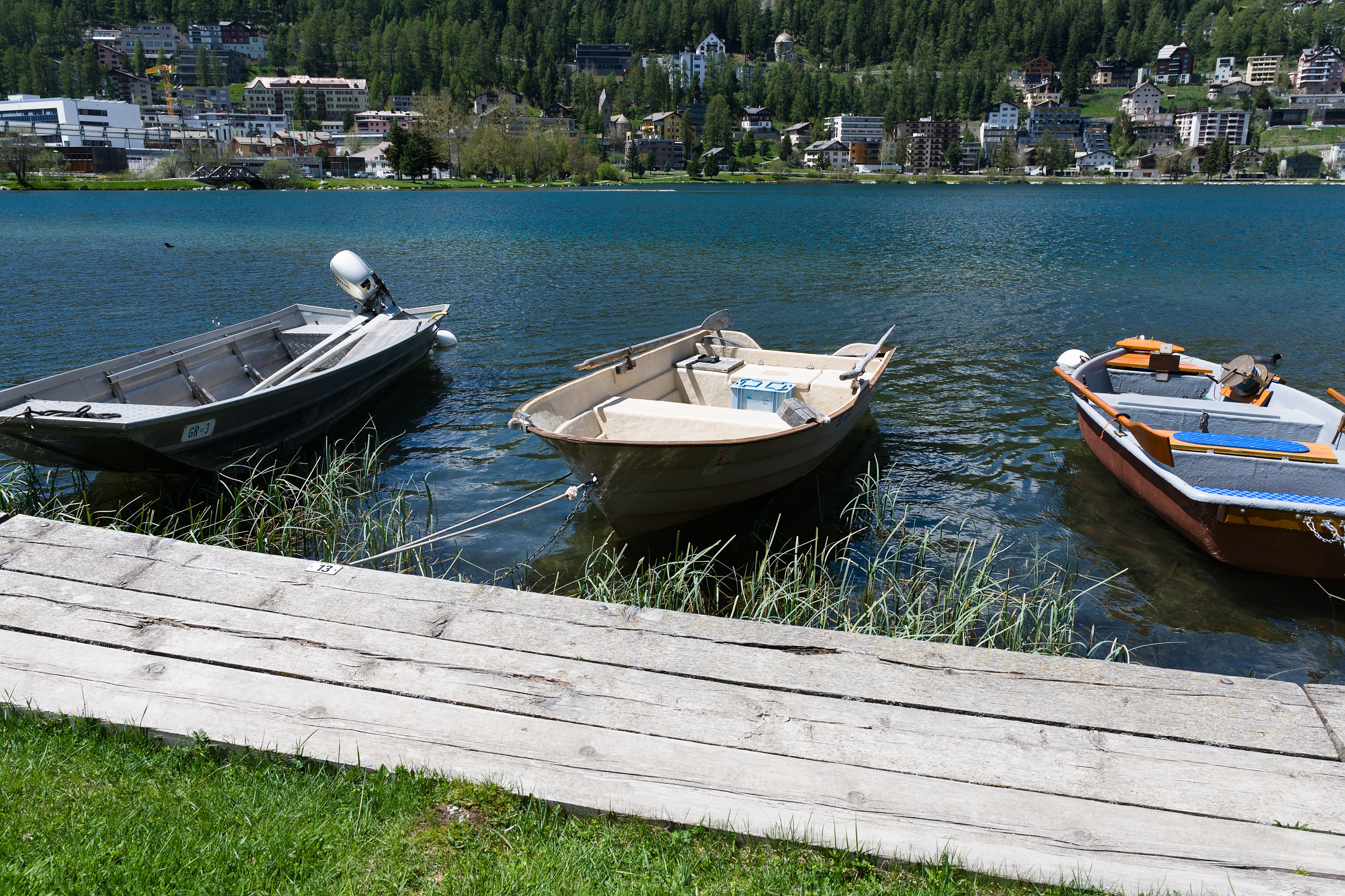Tranquil scene of boats moored near the shore of Lake St. Moritz in a swiss alpine setting.