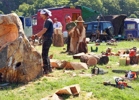 Artisans using chainsaws to craft wooden sculptures outdoors in a park environment.