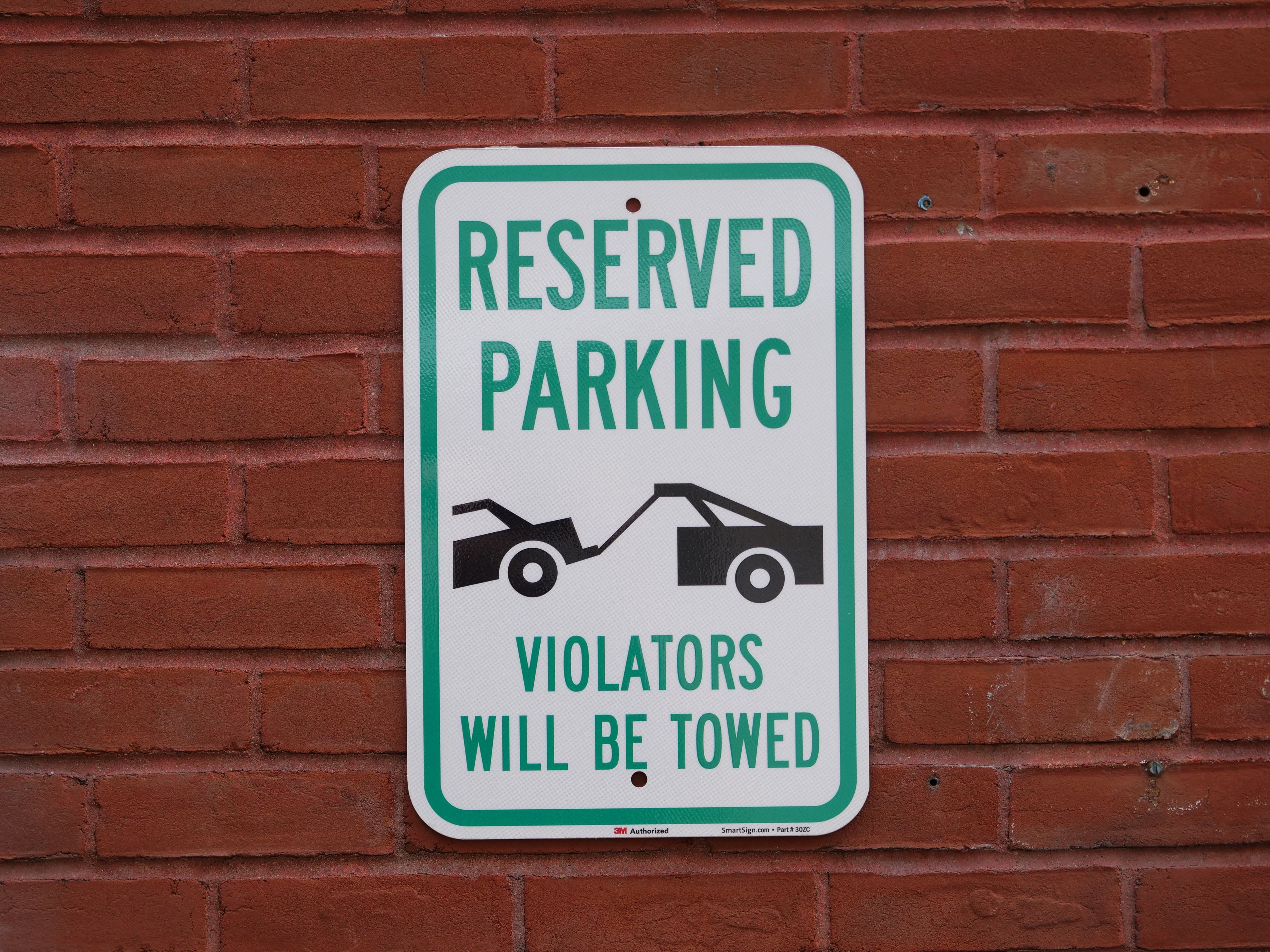 A reserved parking sign on a red brick wall warns that violators will be towed.