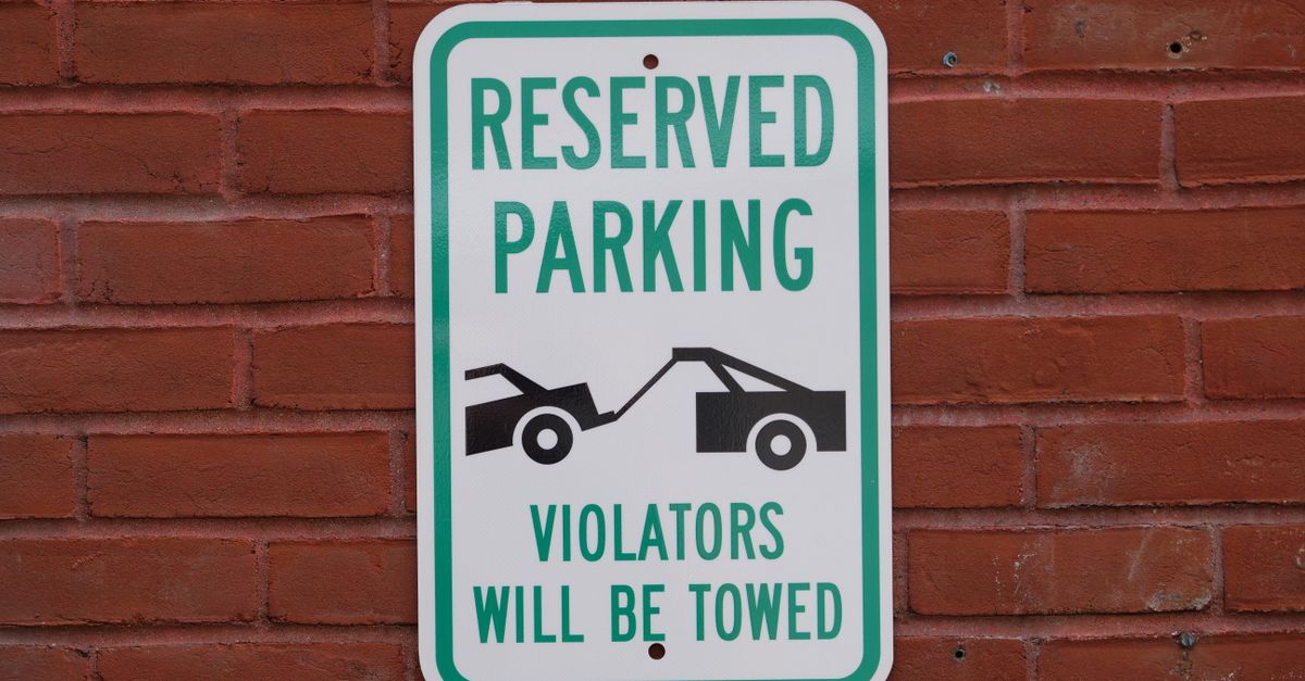 A reserved parking sign on a red brick wall warns that violators will be towed.