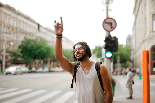 Free Happy ethnic man with backpack hailing taxi on street Stock Photo