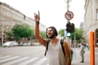 Happy ethnic man with backpack hailing taxi on street