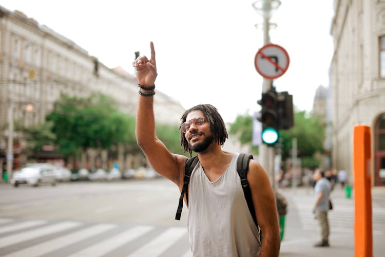 Happy Ethnic Man With Backpack Hailing Taxi On Street