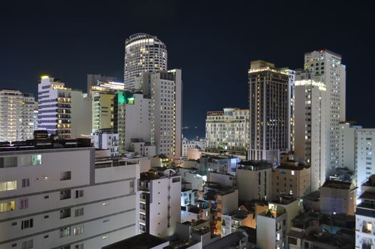 A vibrant city skyline at night with tall illuminated buildings and clear skies.