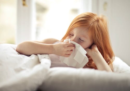 Ill preteen girl wiping snot while resting in bed at home