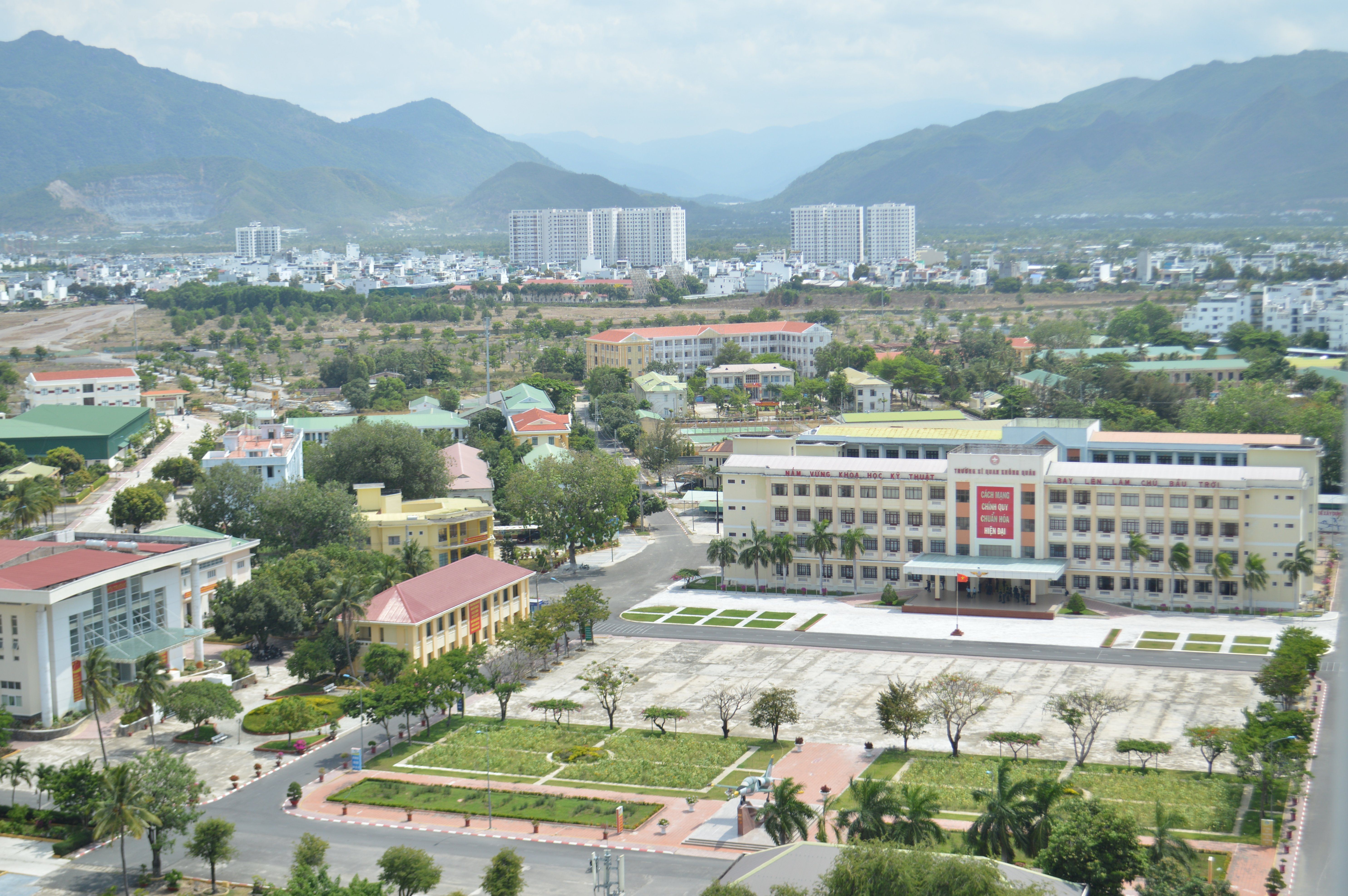 Aerial cityscape showing buildings, roads, and mountains in the background.