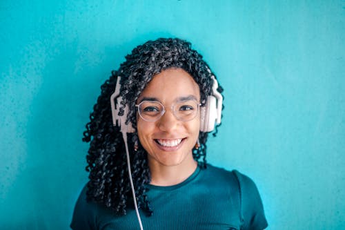 Portrait Photo of Smiling Woman in Black T-shirt ans Glasses Wearing White Headphones