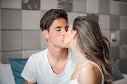 Photo of Man in White Crew Neck T-shirt Kissing Woman in White Tank Top