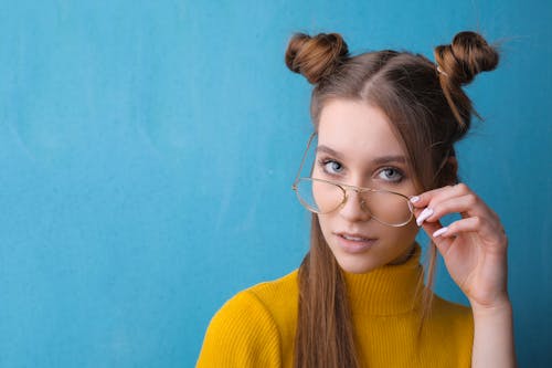 女人穿著黃色的高領毛衣和眼鏡在藍色背景前的肖像照片