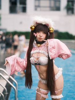 A cosplayer dressed intricately poses by a poolside in an outdoor setting.