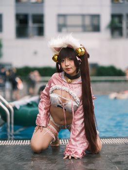 A female cosplayer poses in a pink fantasy costume next to a poolside setting, showcasing detailed outfit and accessories.