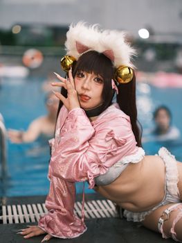 A young woman in a playful cosplay outfit poses by a swimming pool, exuding creativity and fun.