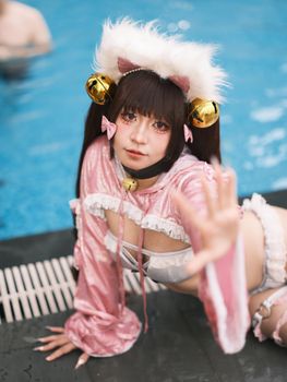 Cosplayer in a pink feline-themed outfit posing dramatically by the pool.