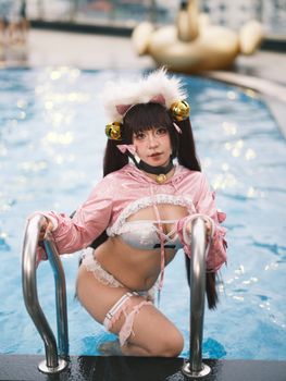 Cosplay model in cat-themed outfit posing at a poolside with a playful backdrop.