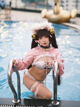 Cosplay model wearing a pink costume poses confidently by the poolside.