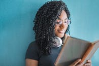 一位卷发的年轻女子戴着耳机在室内看书，面带微笑