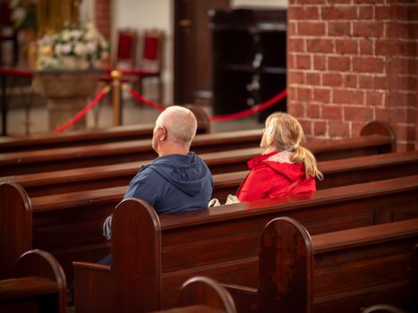 A mature couple sits in wooden pews, reflecting in a serene church interior.