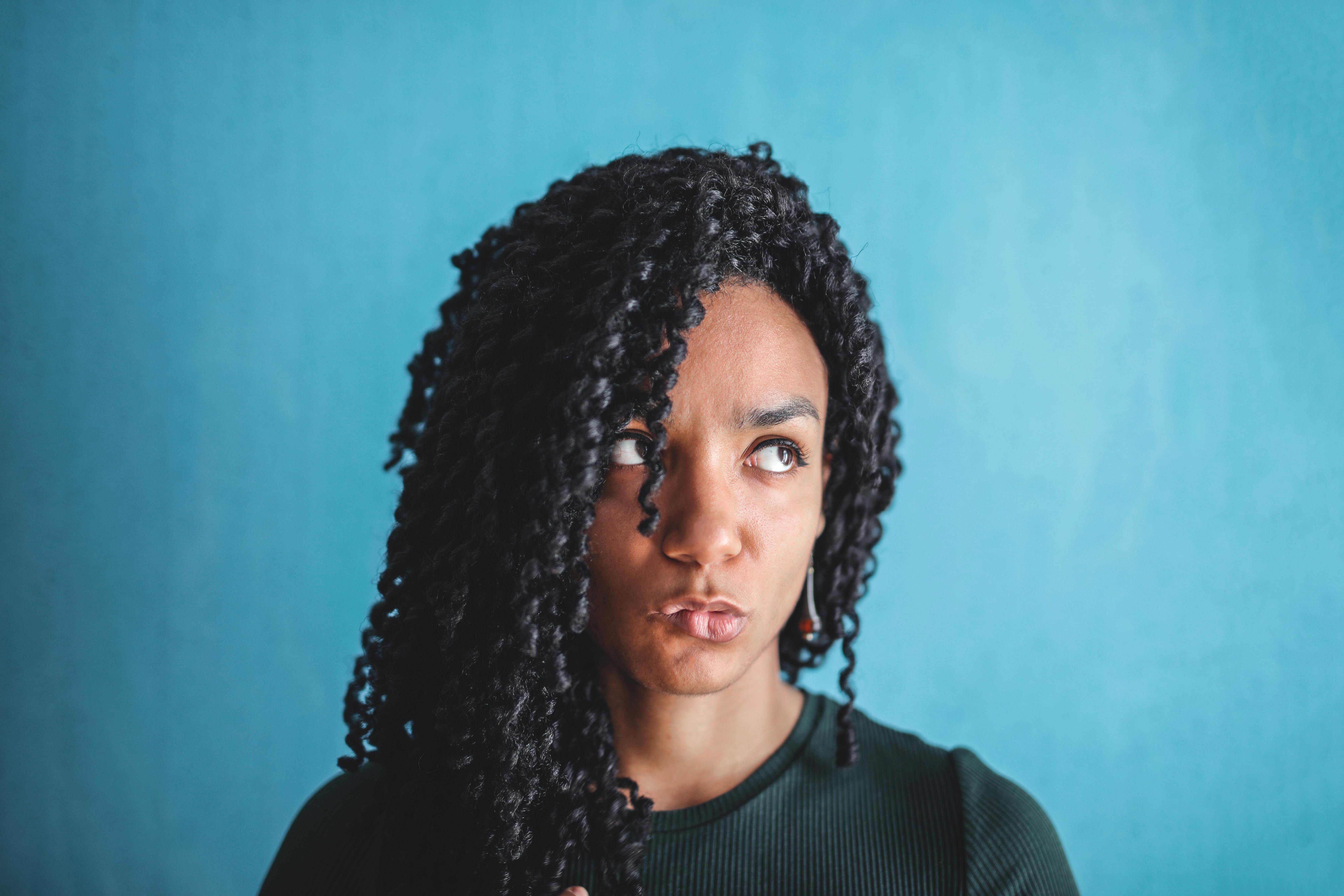 Close-up portrait of a young woman with curly hair against a blue background.