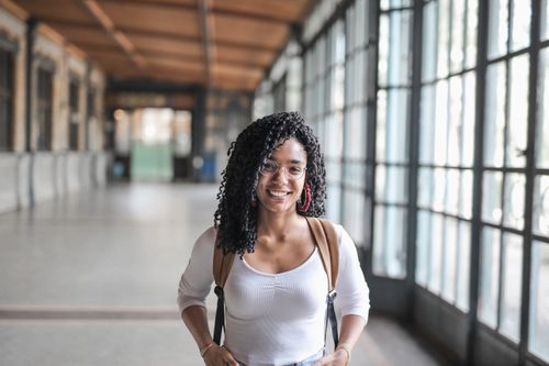 Free Happy young woman with curly hair and glasses smiling in a sunlit hallway. Stock Photo