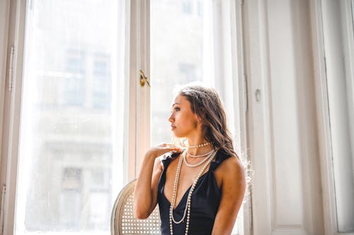 Woman in Black Sleeveless Dress Standing Beside White Framed Glass Window