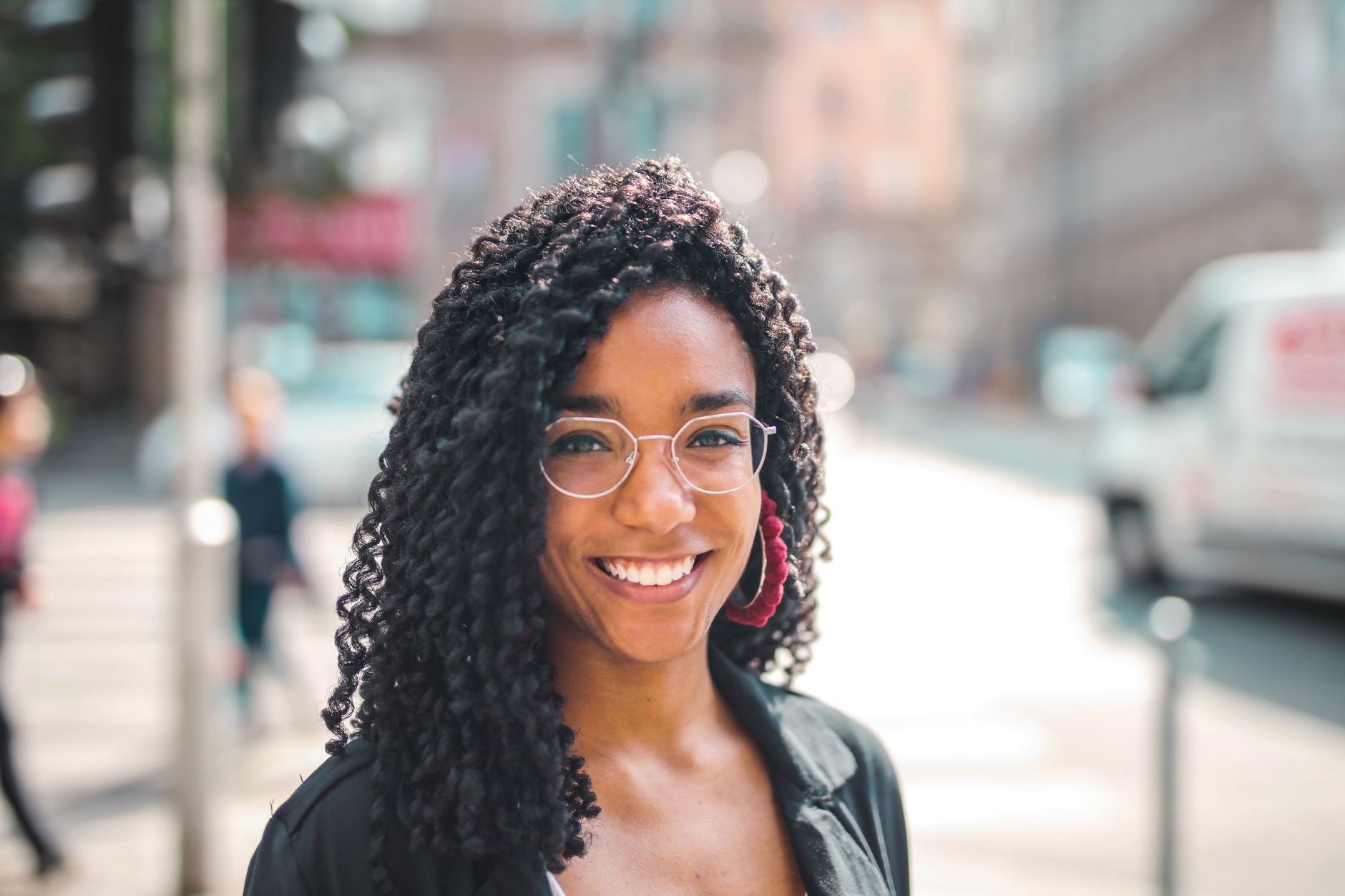 How to Choose Eyeglasses That Reflect Your Personality and Style 1 Attractive young woman with curly hair and eyeglasses smiling on a sunny day in the city.