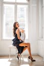 一位时尚的年轻女子在光线充足的房间里，坐在椅子上摆出优雅而时尚的姿势