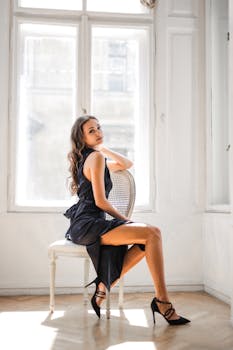 一位时尚的年轻女子在光线充足的房间里，坐在椅子上摆出优雅而时尚的姿势