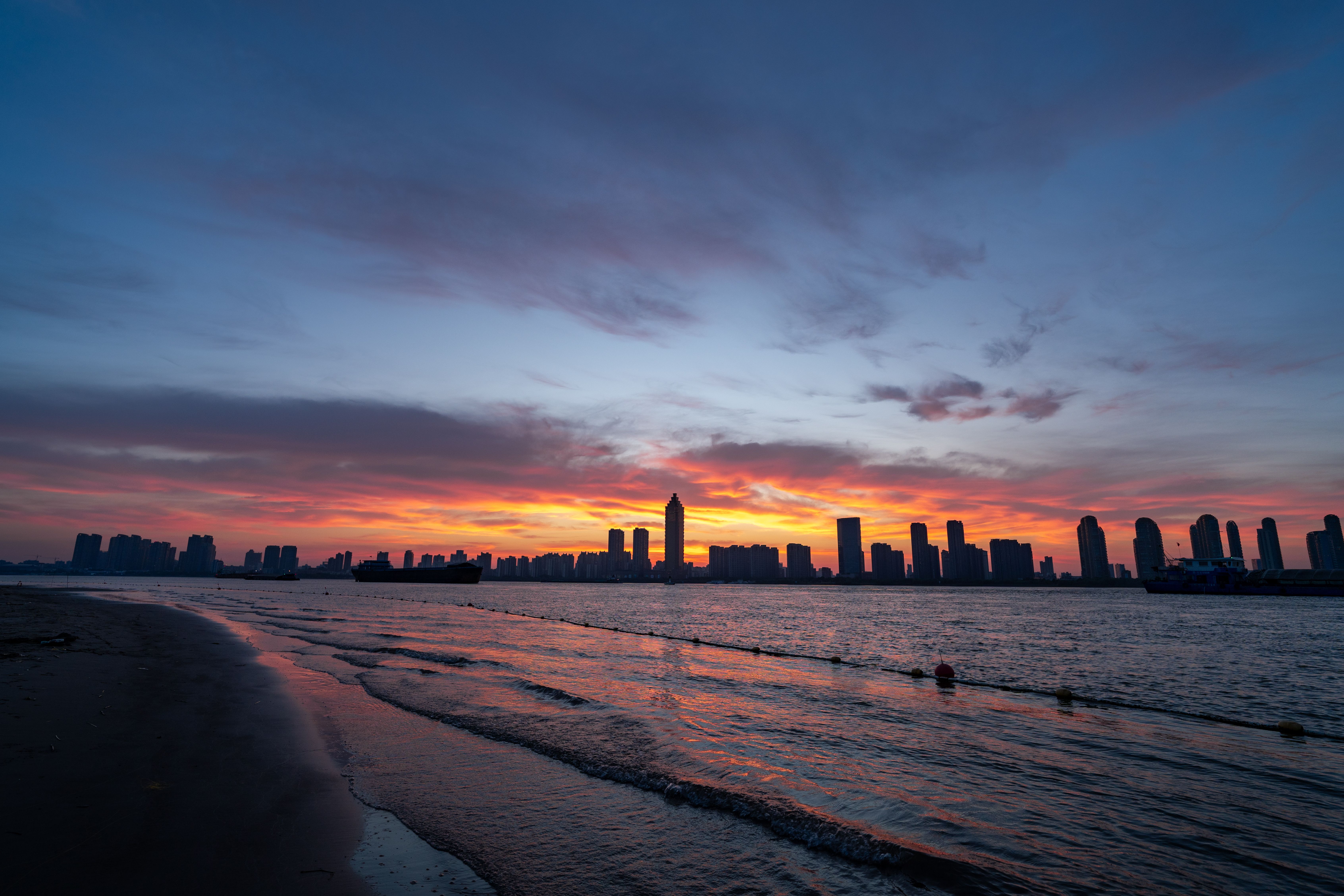 Sunset Over Modern City Skyline Viewed from Beach · Free Stock Photo