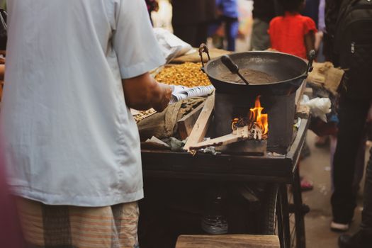 Street vendor preparing food over an open flame in a bustling outdoor market.