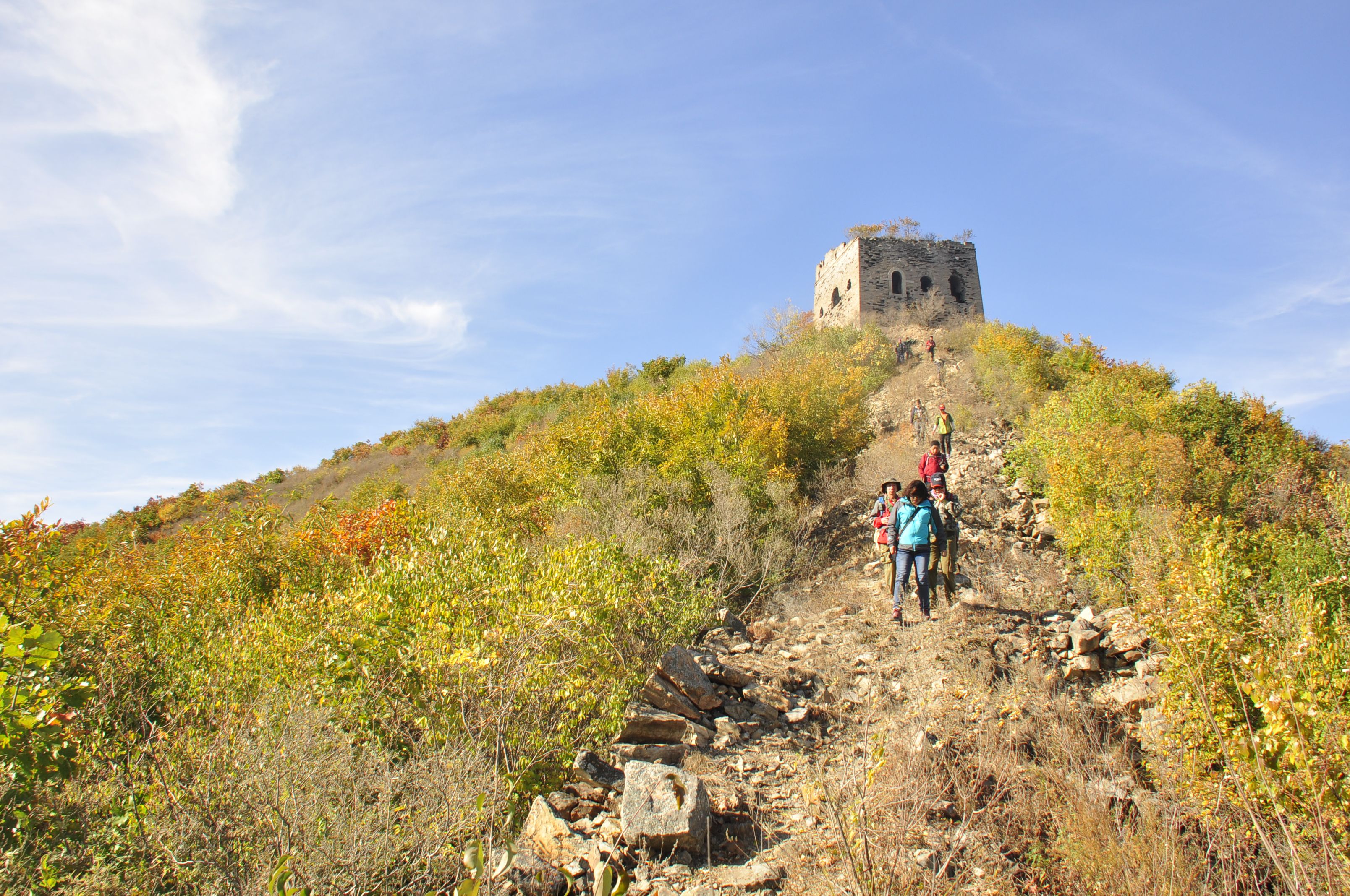 Group of hikers ascending a trail towards an ancient stone structure on a hilltop surrounded by fall foliage.