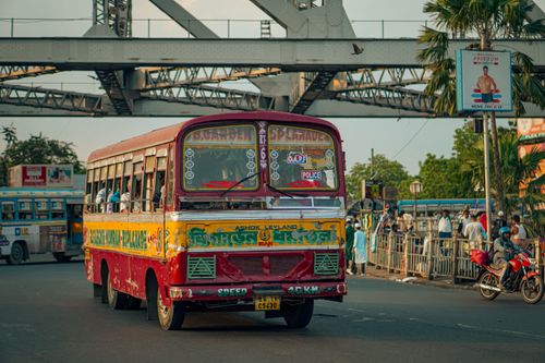Free A colorful local bus travels through busy Kolkata streets with Howrah Bridge in the background. Stock Photo
