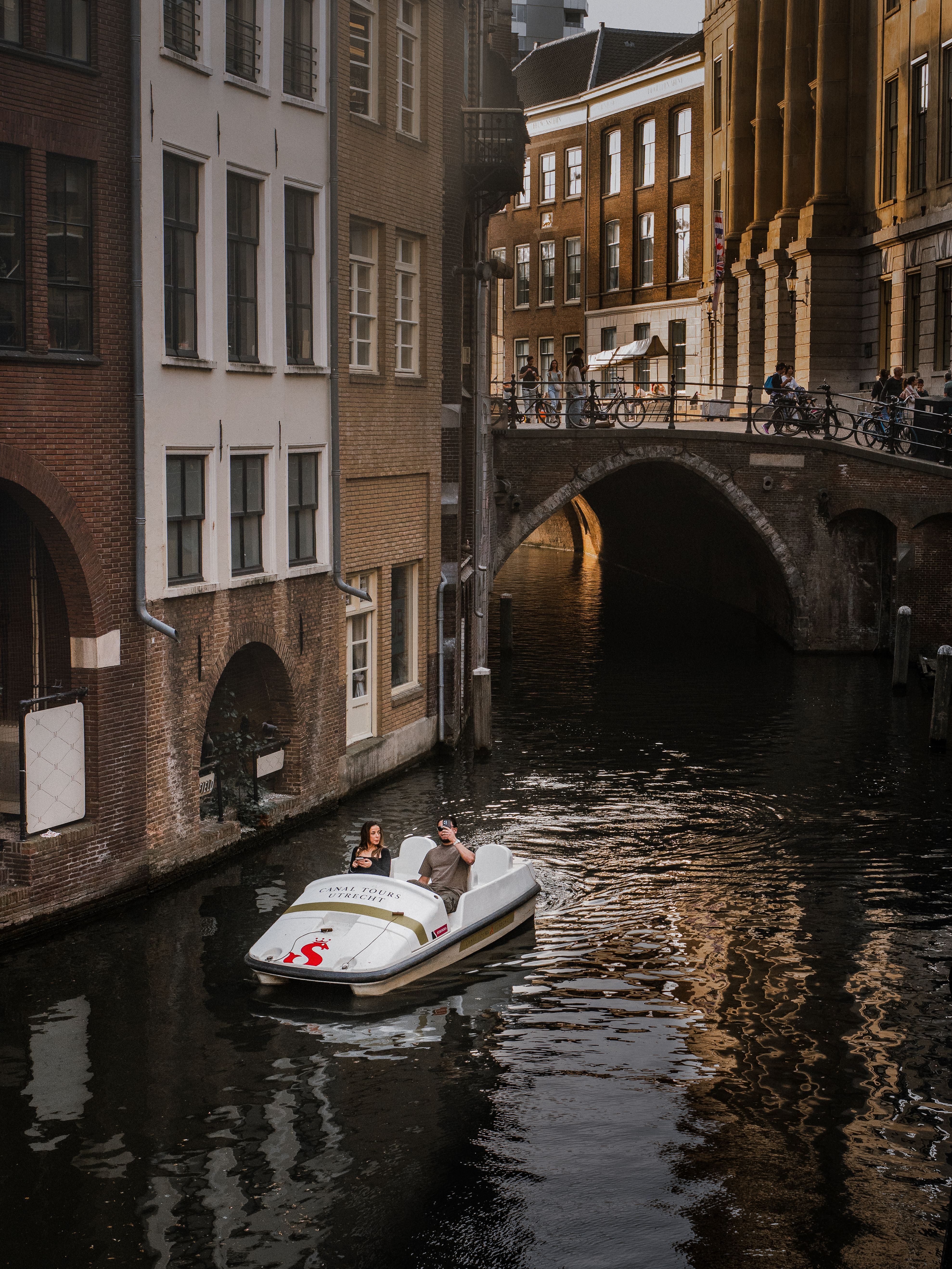Couple enjoying a pedal boat ride through a picturesque European canal with historic architecture.