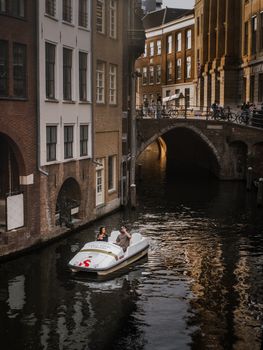 Couple enjoying a pedal boat ride through a picturesque European canal with historic architecture.