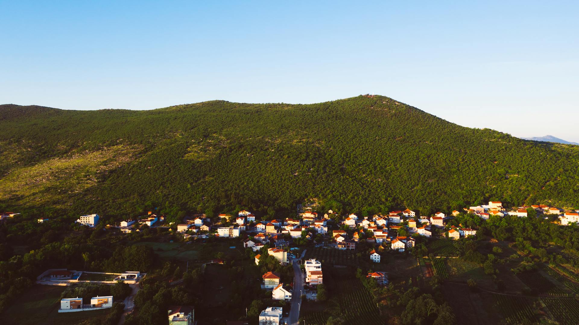 A vibrant aerial view of a small town nestled in Bosnia's green mountains under a clear blue sky.