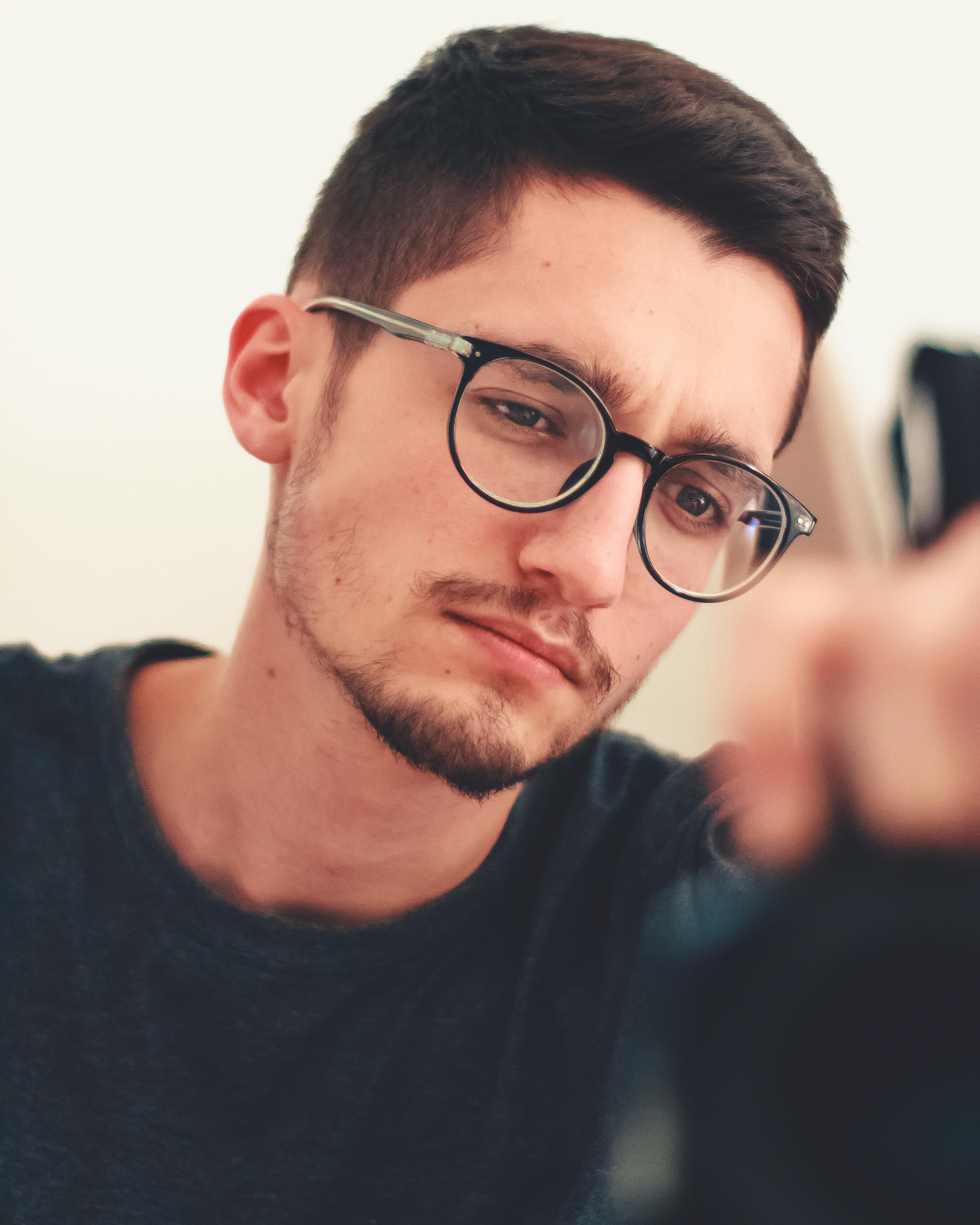 这是一幅在室内拍摄的肖像，画面中一位戴眼镜的年轻人正在沉思