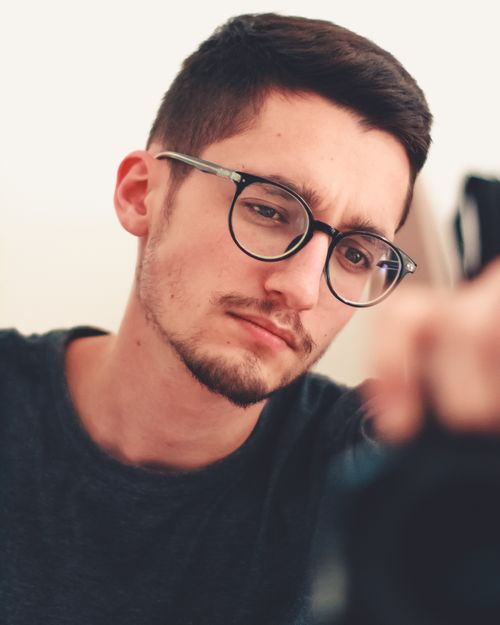 Free Portrait of a thoughtful young man wearing eyeglasses, captured in a pensive moment indoors. Stock Photo