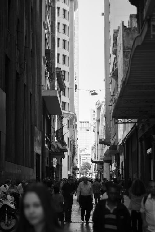 Grayscale Photo of People Walking on Street Between Buildings