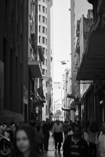 Black and white photo of a bustling city street lined with historic buildings and a crowd of people.