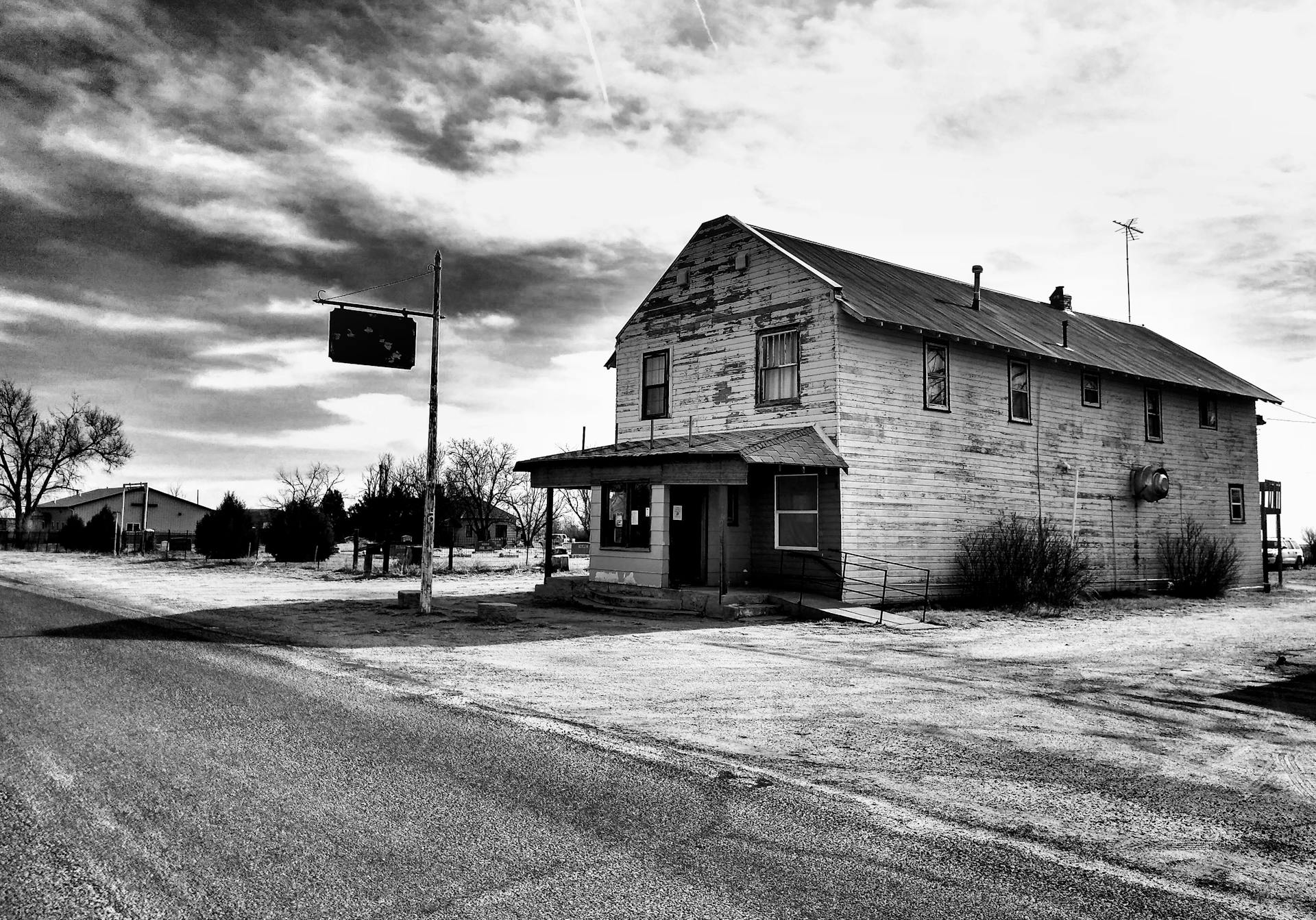 Black and white photo of an abandoned wooden house in a barren rural landscape.