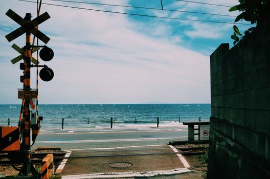 Coastal view from a railway crossing overlooking the serene Tokyo Bay with a clear blue sky.