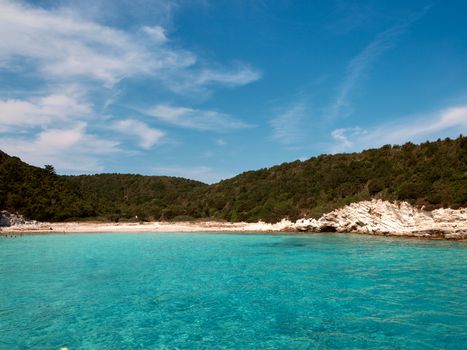Capture of a tranquil beach with turquoise waters and lush green cliffs in Greece.