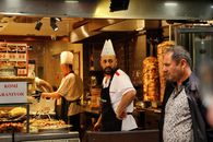 A vibrant scene inside a Turkish döner kebab shop with chefs and a patron.