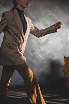 Fashionable woman in plaid jacket walking in studio with dramatic lighting.