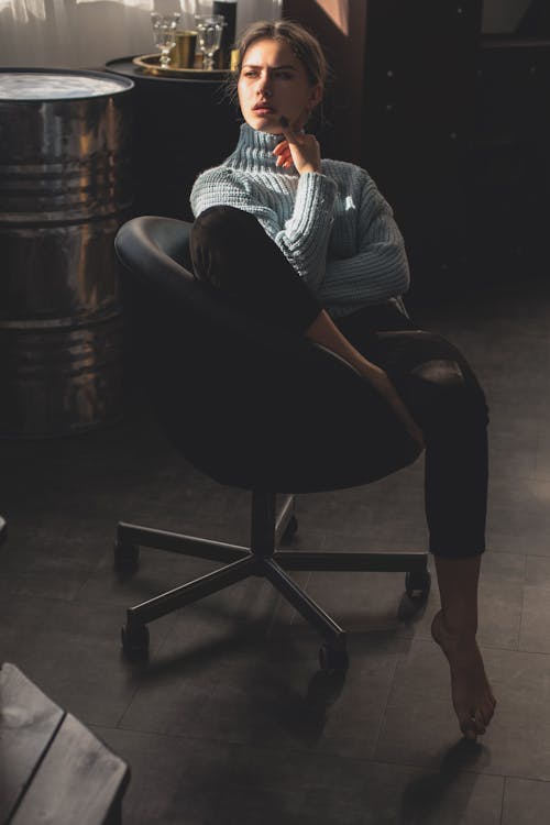 Woman in Blue Sweat  Shirt and Black Pants Sitting on Black Leather Chair