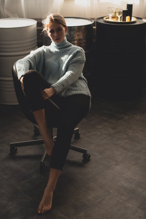 女人穿着蓝色的毛衣和黑色的裤子，坐在黑色的办公室转椅上