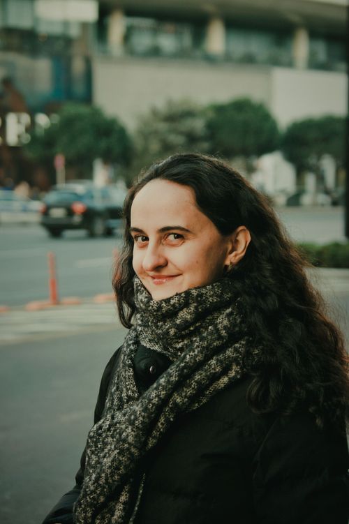 Free Young woman with curly hair smiling in a city street, wearing a winter scarf. Stock Photo