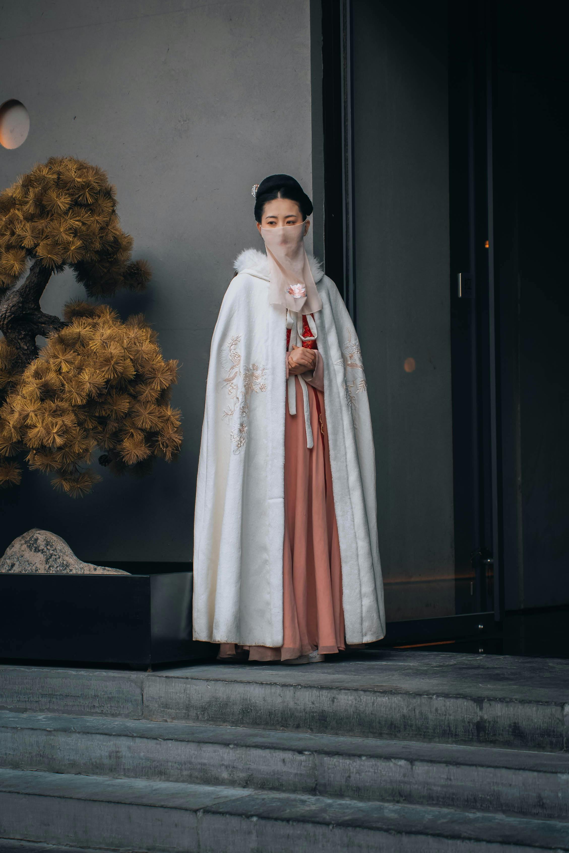 A woman wearing traditional Chinese clothing stands elegantly outside a building, embodying cultural heritage.