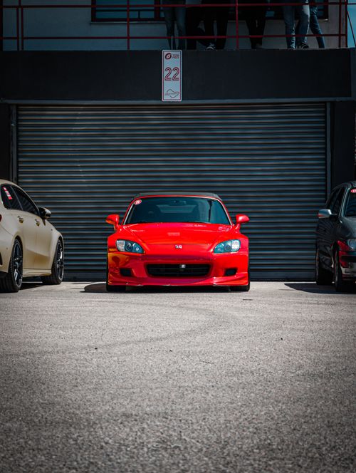 Free Front view of a red sports car parked between two cars on a sunny day. Stock Photo