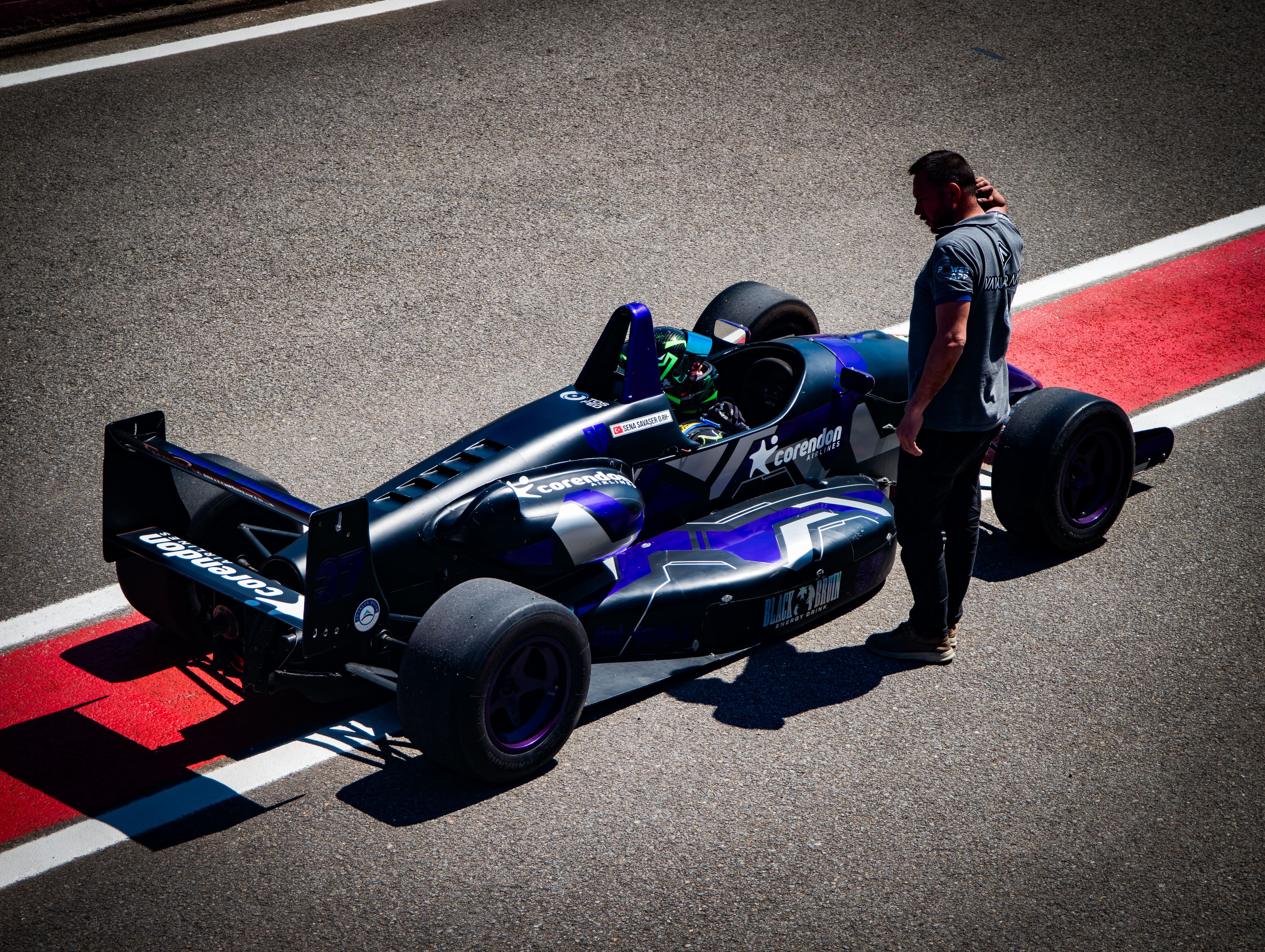 A Formula One race car on the track with a driver and pit crew member during the day.