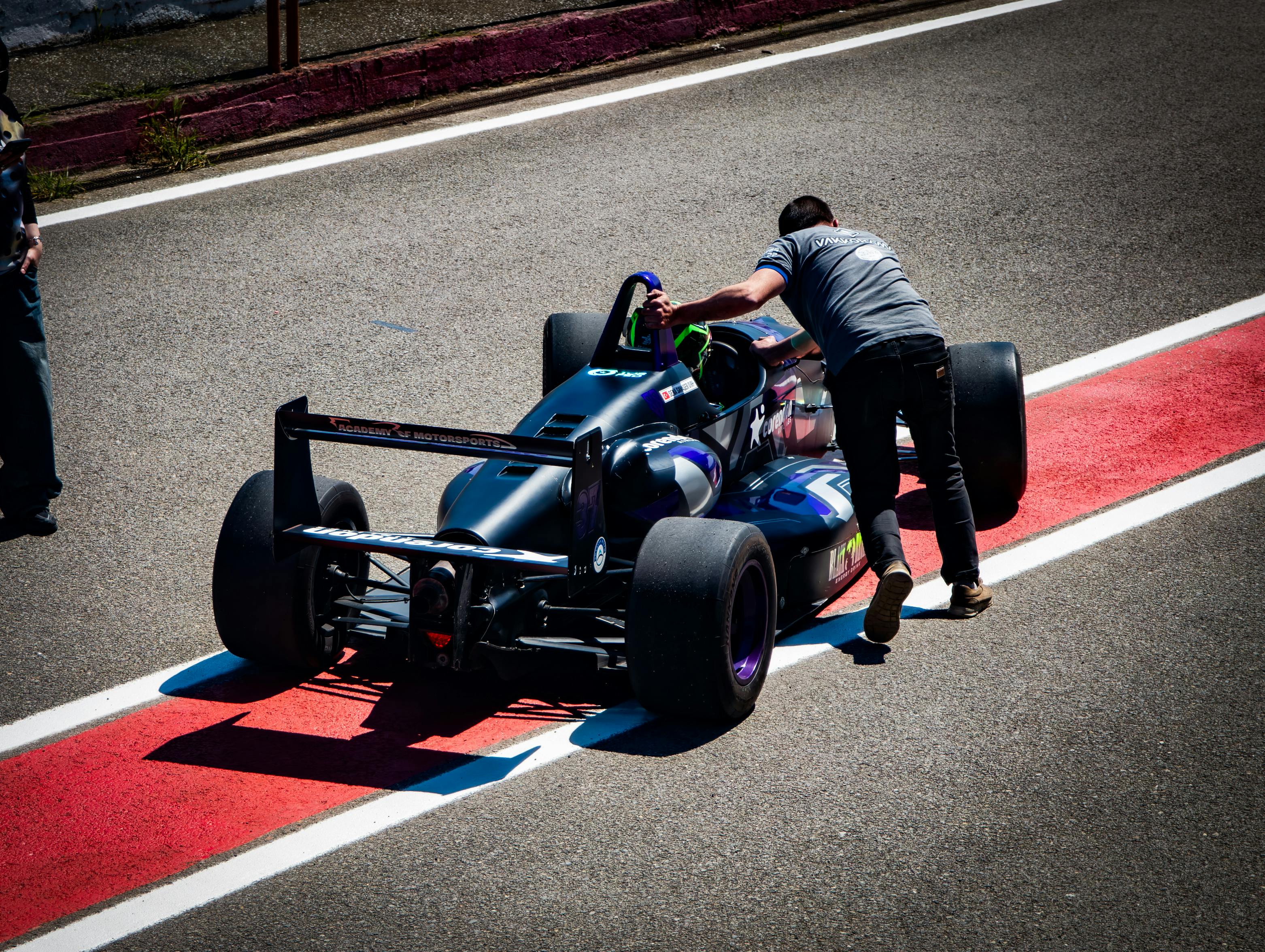 An exciting scene of a crew member pushing a race car on the track under sunlight.